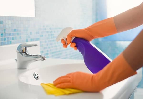 Person wearing rubber gloves using cleaning spray on a basin