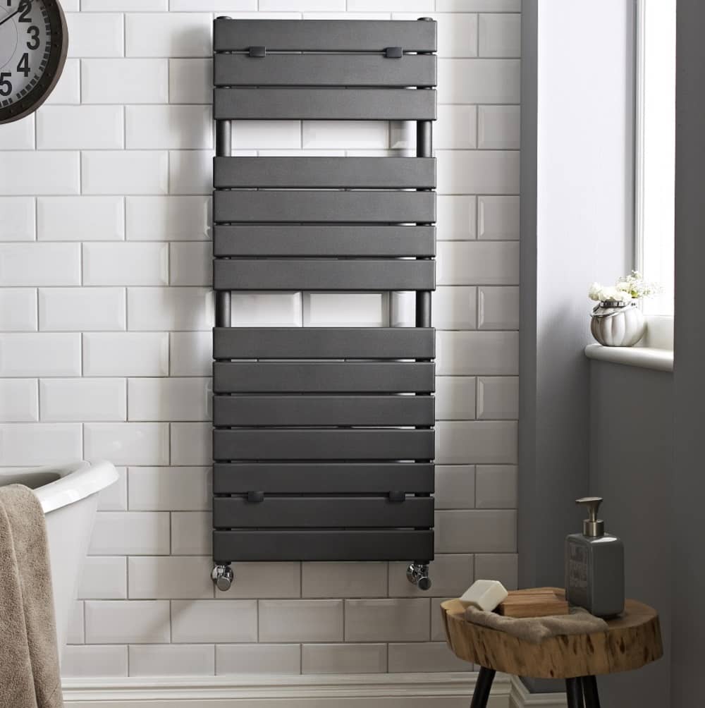 Grey heated towel rail on white metro tiled wall with grey adjacent wall. Grey heated towel rail on white metro tiled wall with grey adjacent wall.
