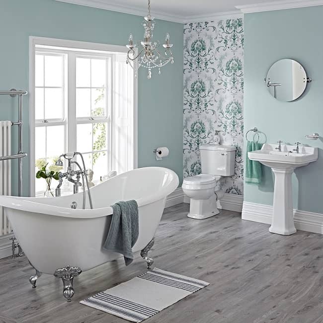 Traditional bathroom suite with freestanding bath, toilet and cistern, and pedestal basin, with round mirror.