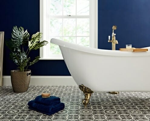 A white freestanding bathtub and gold bath tap in a blue bathroom