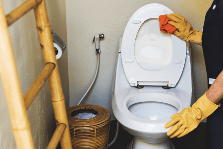 housekeeper-cleaning-a-toilet a cleaning lady cleaning a toilet with a cloth