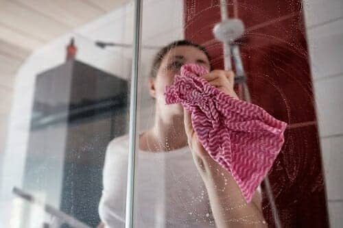 a woman cleaning a shower screen with a pink cloth