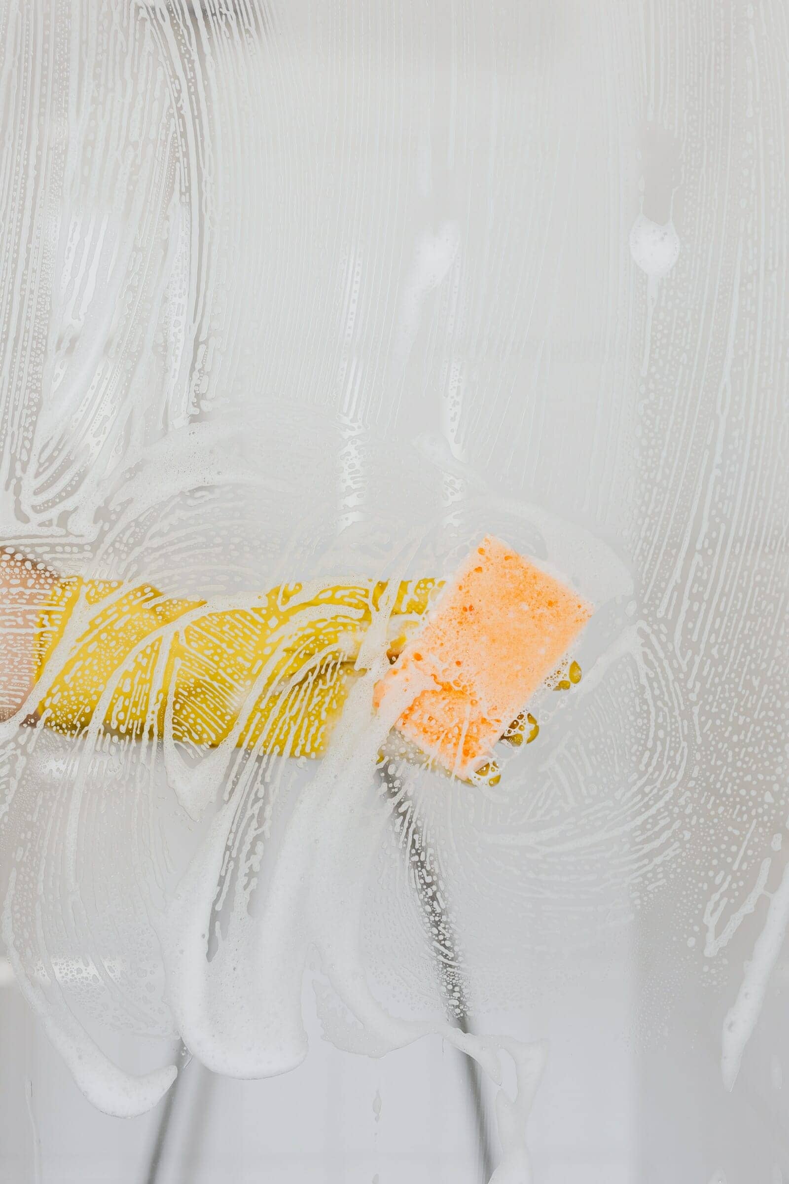 Cleaning a shower screen with sponge and yellow rubber gloves
