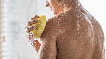 Man reinigt zichzelf onder de douche met gele spons