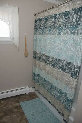 Multicoloured shower curtain hung on railing nearby blue bath mat