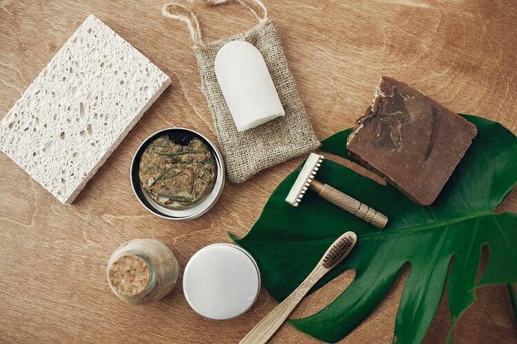 Sustainable Bathroom Products - Zero waste, plastic free beauty essentials. Natural soap, shampoo bar in metal can, reusable razor, crystal eco deodorant, toothpaste, sponge, bamboo toothbrush, ubtan on wooden background
