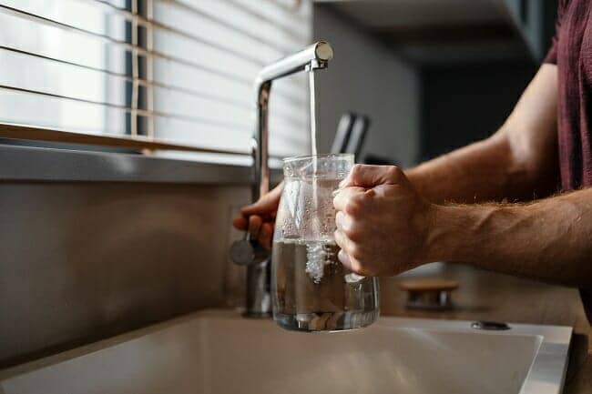 Close up of a man pouring water in the jug from a tap while standing at the kitchen sink