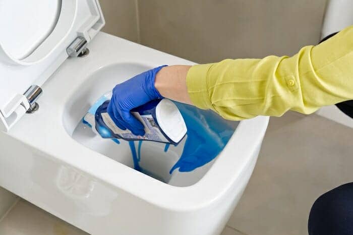 Wall mounted toilet being cleaned with blue cleaning liquid